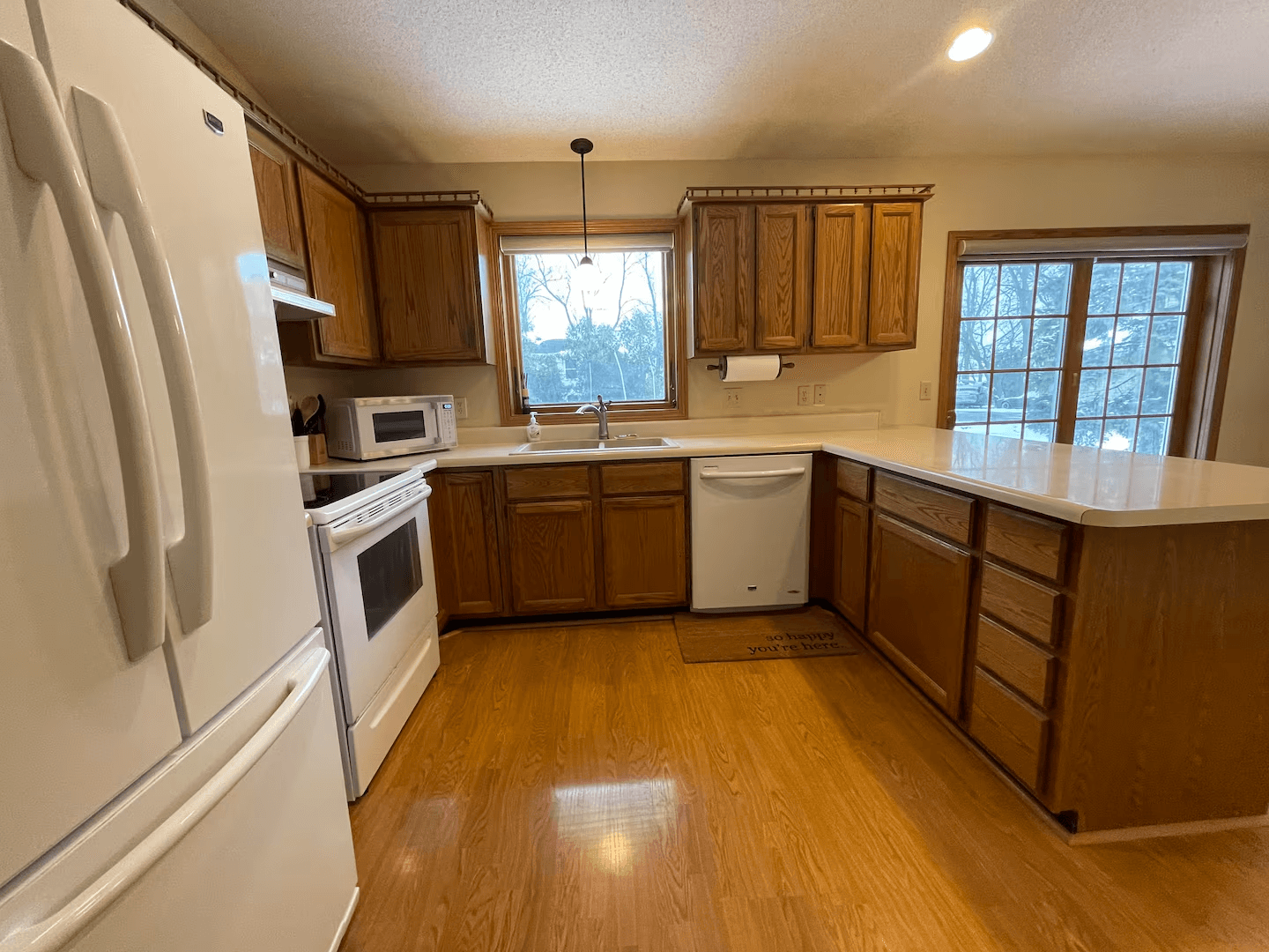A traditional kitchen with warm wood cabinets, white countertops, and a white refrigerator.