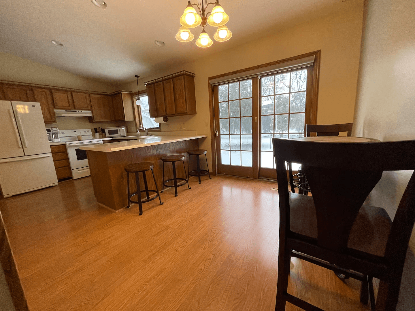 A modern open-concept kitchen and dining area with light wood flooring, a kitchen island with bar stools, and a dining table with chairs.