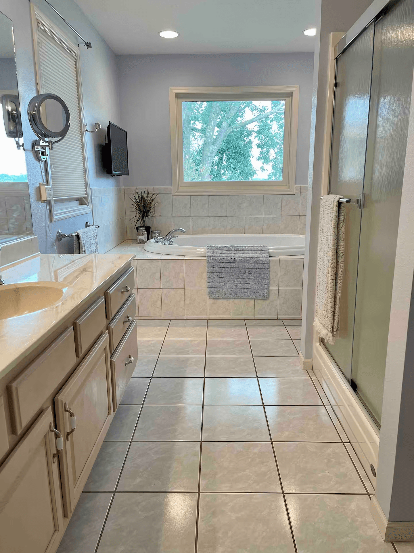 Light-filled bathroom with soaking tub, glass-enclosed shower, vanity with sink, and tiled floor.