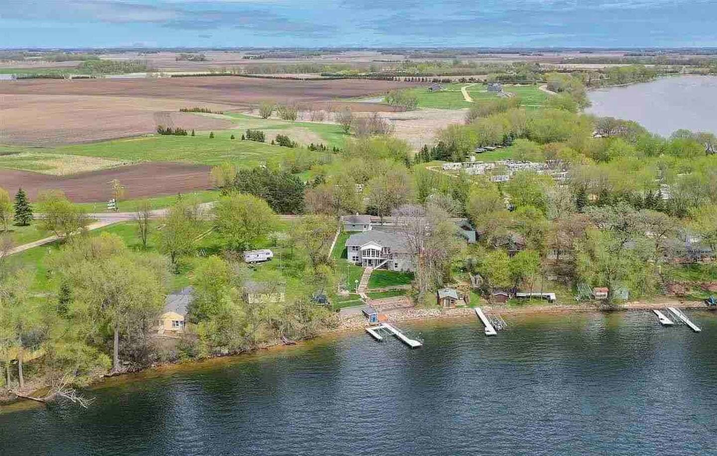 An aerial view of a lake shore with green trees, several homes, and docks.