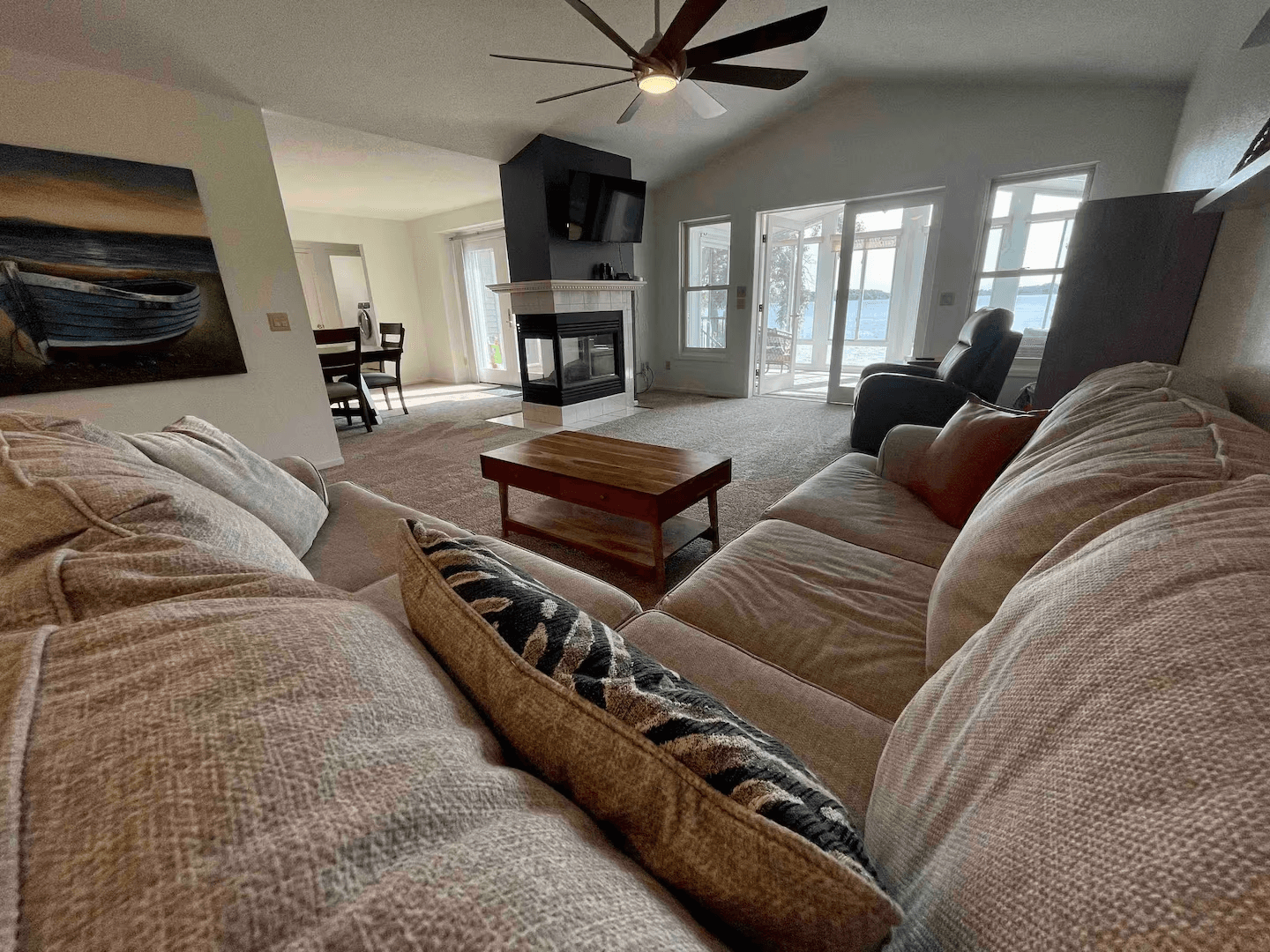 View from living room sofa of dining area, double-sided fireplace, flat-screen TV, and entrance to four-season room.