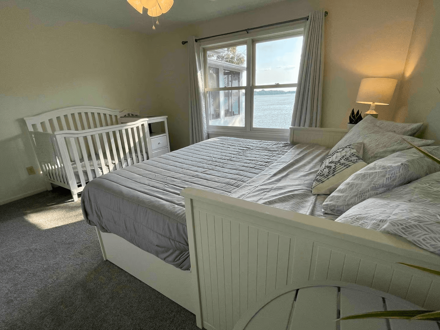 Tranquil, softly lit bedroom decorated in neutral tones features a bed, crib, and window with lake views.
