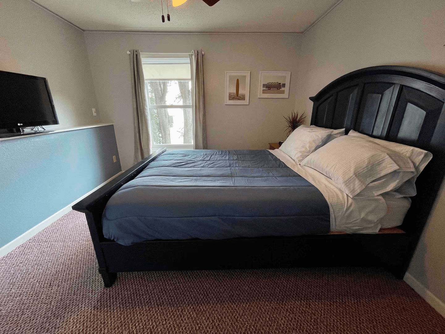 Bedroom with wooden bed frame painted black facing a flat-screen TV.