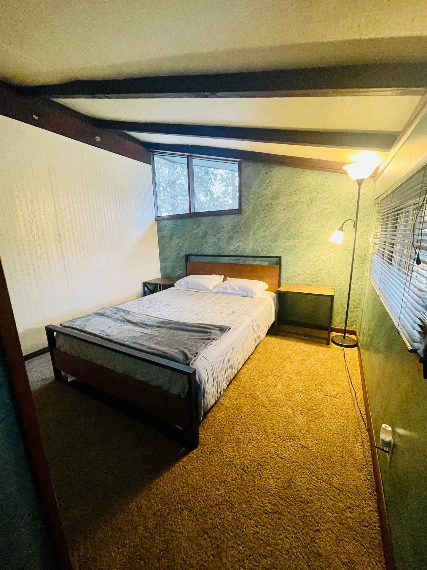Cozy bedroom with a bed, floor lamp, and open-beam ceiling.