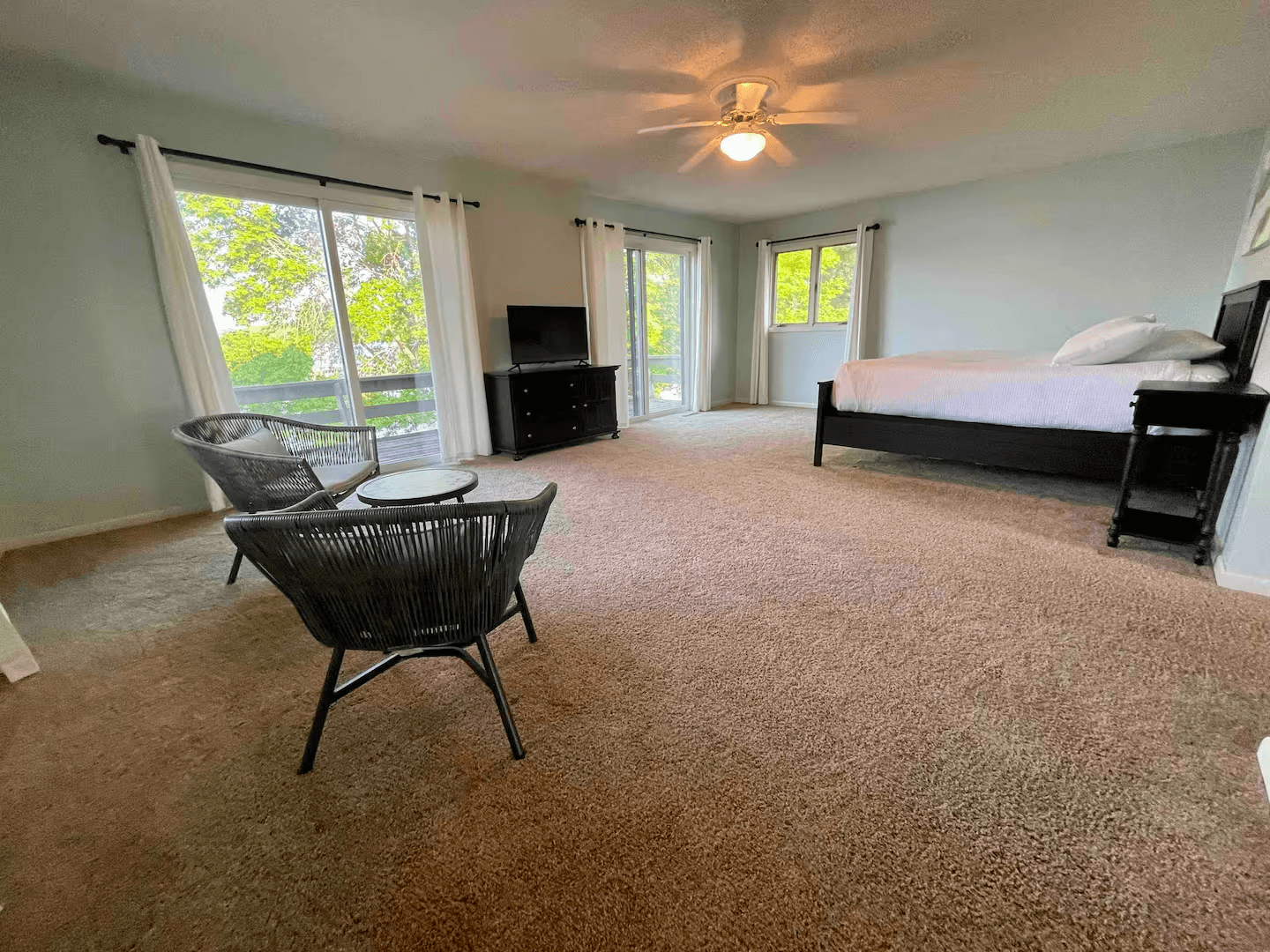 A large bedroom with lake views, seating area, flat-screen TV, and ceiling fan.