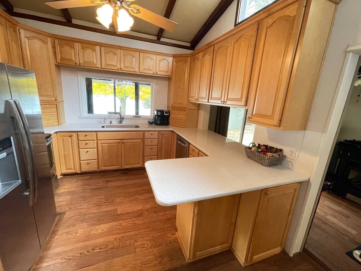 Kitchen with stainless refrigerator, light wooden cabinetry, and ceiling fan.