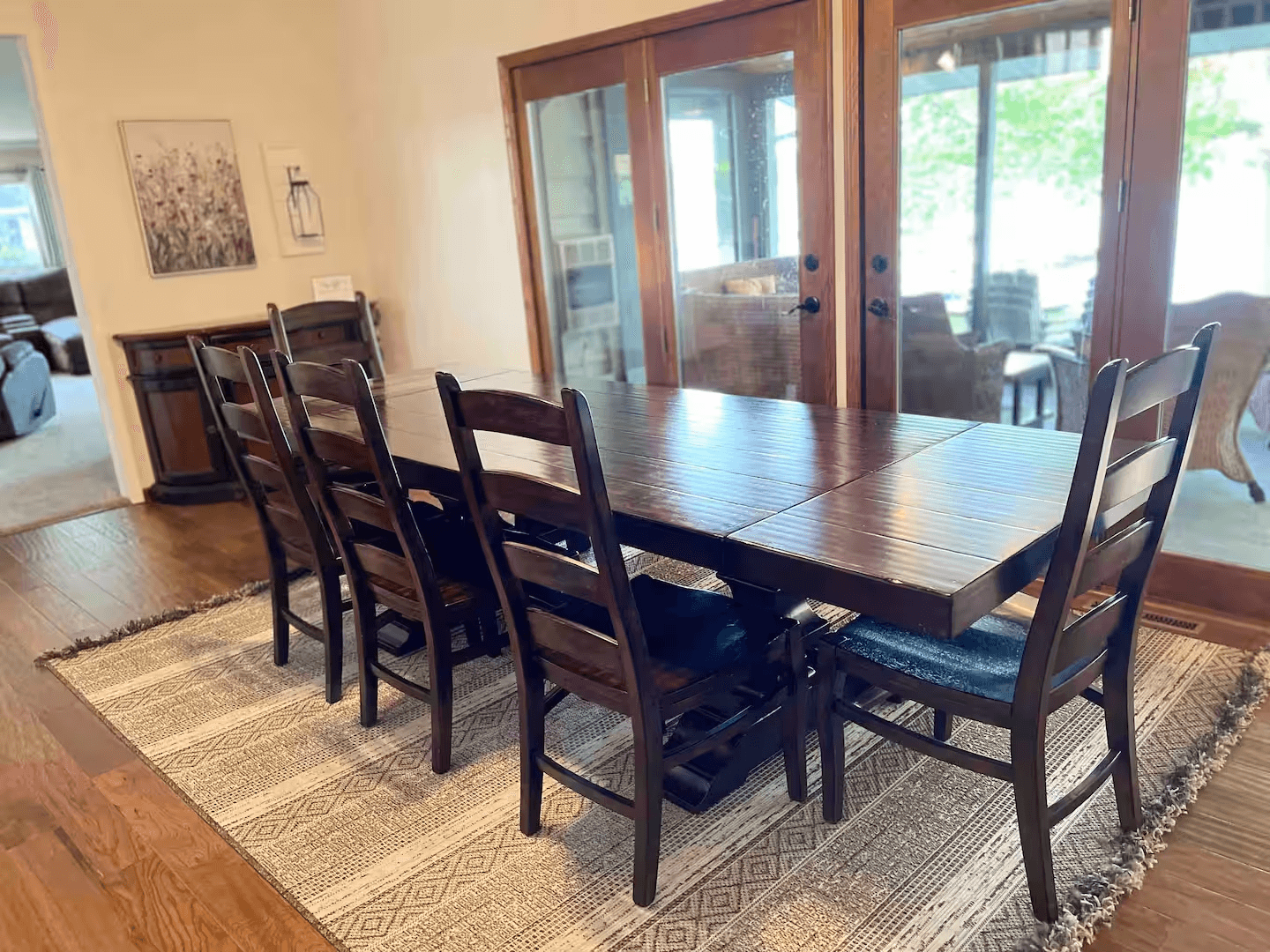 Dining area with long table and matching chairs with view of four-season room.