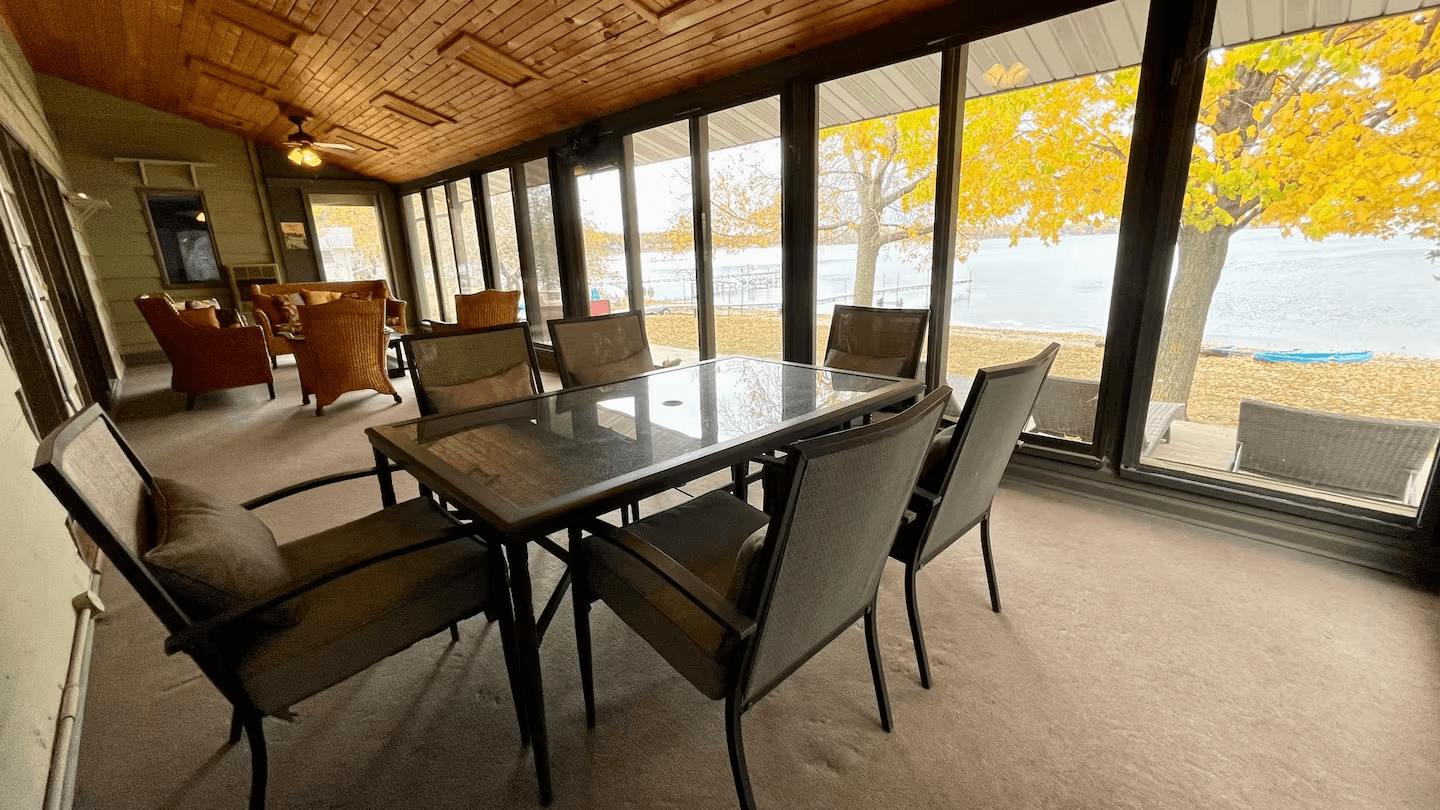 Spacious four-season room with plenty of seating, including a table for meals, and expansive lake views.